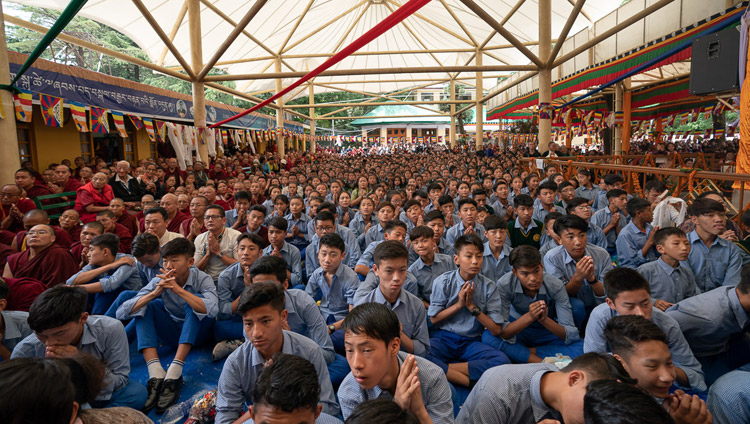 Gli studenti tibetani, seduti nel cortile, assistono alla Cerimonia di offerta di lunga vita per Sua Santità il Dalai Lama dai maxi schermi. Dharamsala, India, il 17 maggio 2019. Foto di Tenzin Choejor
